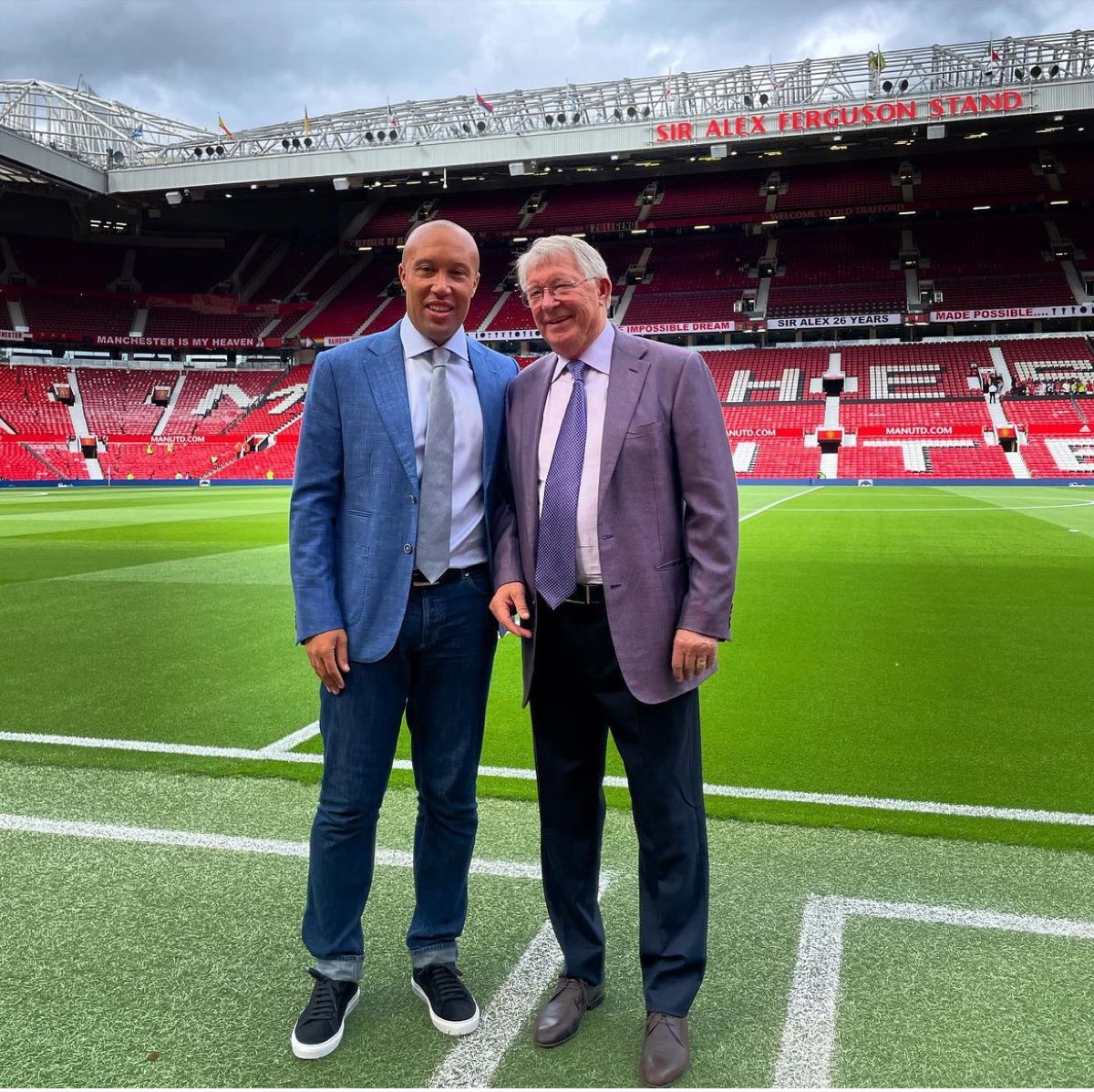 Mikaël Silvestre with Sir Alex Ferguson on the pitch at Old Trafford, beneath the Sir Alex Ferguson Stand